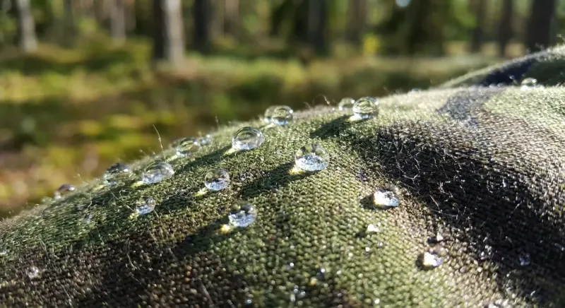 Gouttes d'eau formant des perles sur le textile d'une veste de chasse après un traitement déperlant.